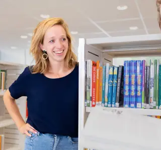 Vrouw korter blond haar en vrouw bruin haar krullen bij boekenrek